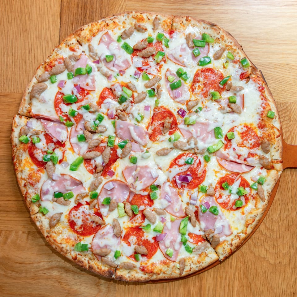 A Numero Uno Pizza with pepperoni, ham, sausage, green peppers, and red onions on a wooden board.