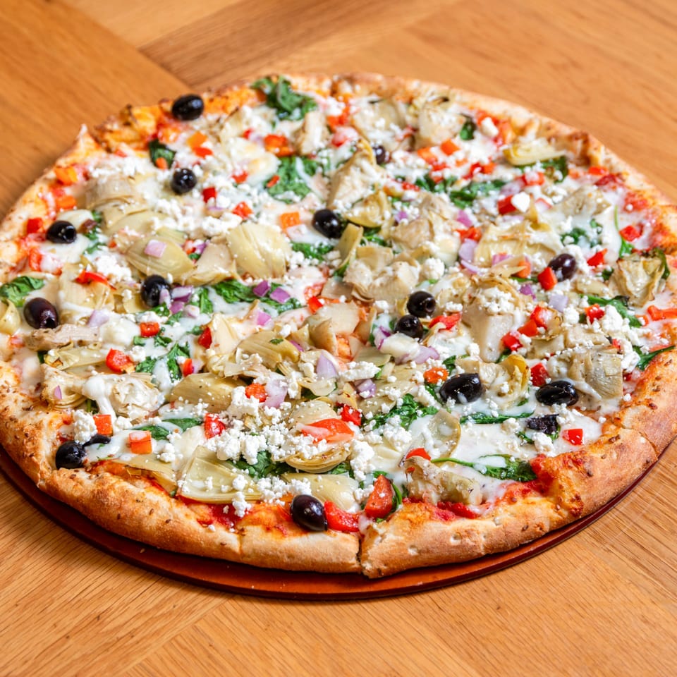 Numero Uno Pizza with artichokes, spinach, olives, red peppers, and feta cheese on a wooden board.