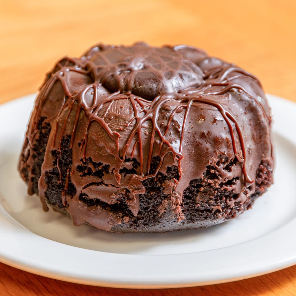 A rich chocolate bundt cake with a thick chocolate glaze on a white plate.