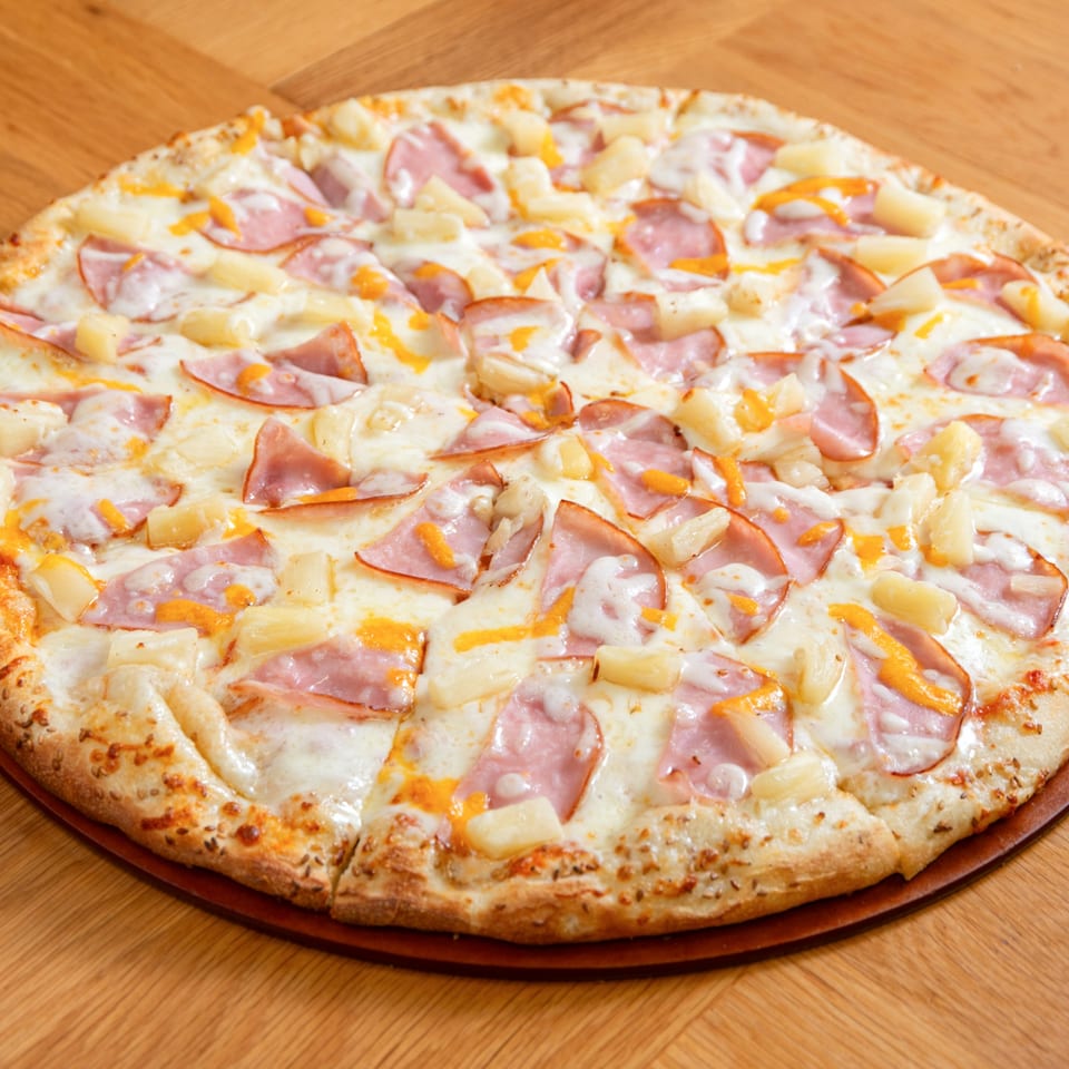 A whole Numero Uno Pizza with ham, pineapple, and melted cheese on a wooden table.
