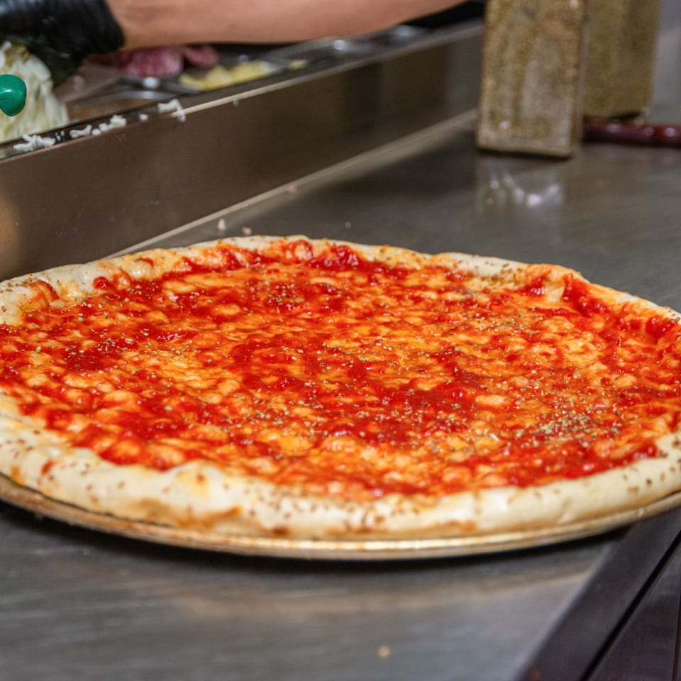 Uncooked Numero Uno Pizza with red sauce and herbs on a metal tray in a kitchen.